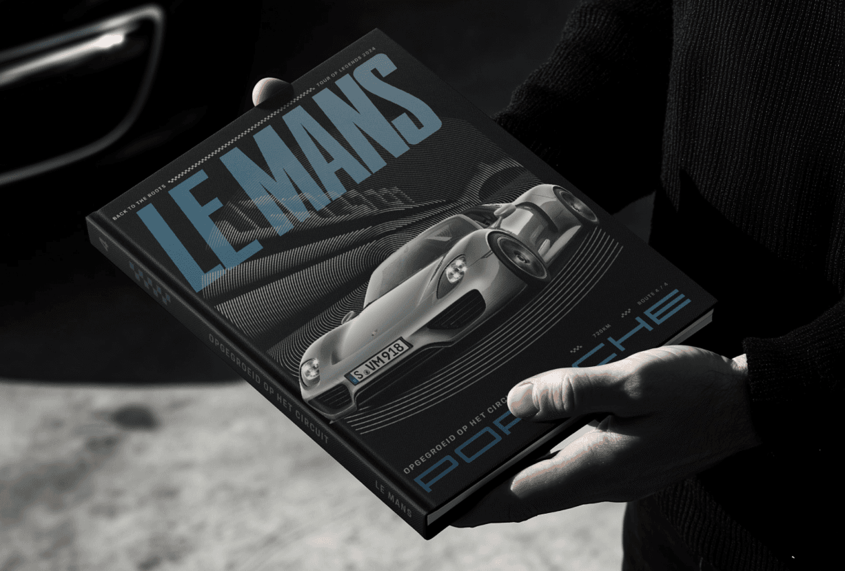 Hands holding a "Le Mans" hardcover book featuring a silver Porsche sports car on the cover