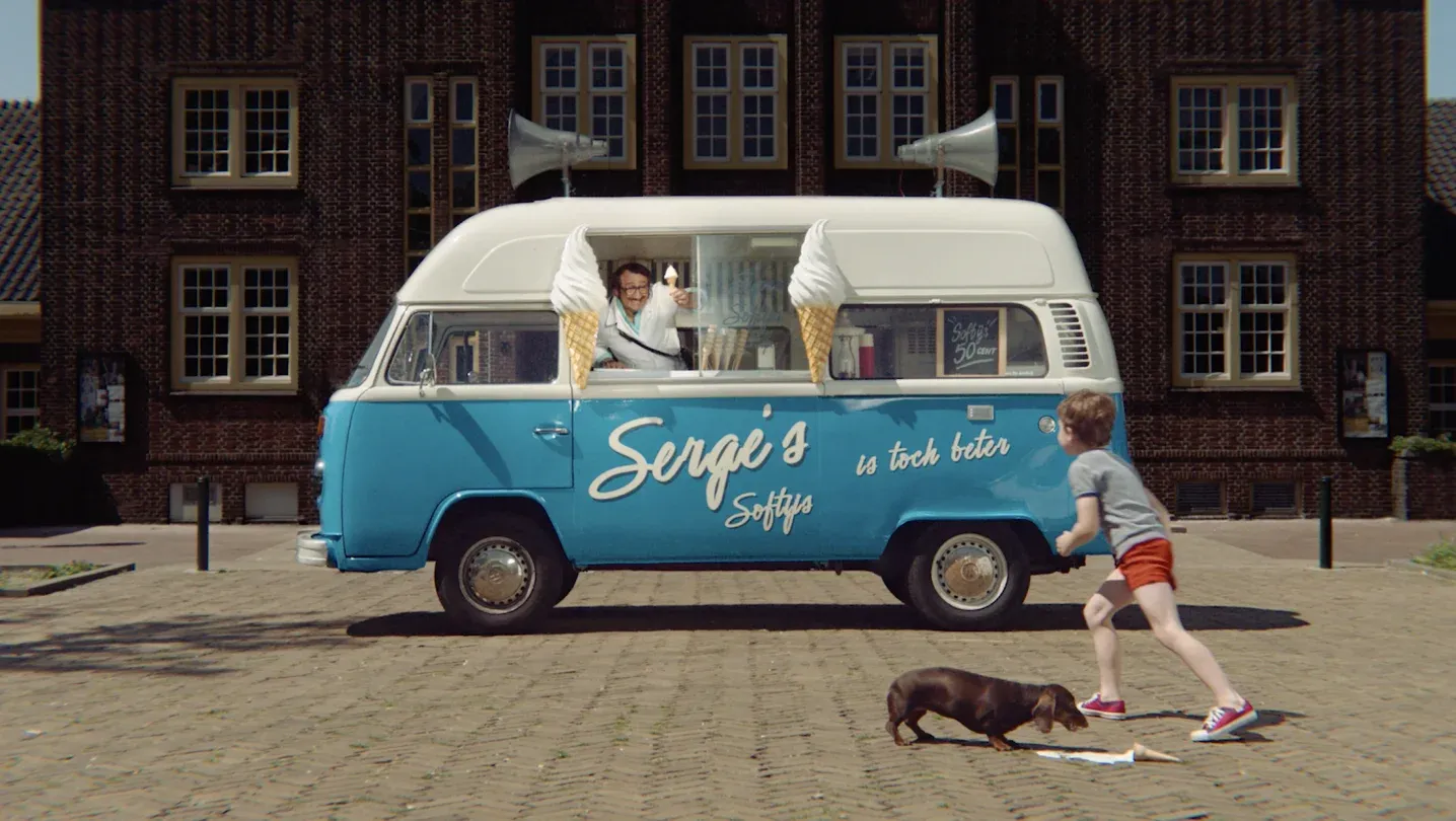 A nostalgic scene of a blue and white vintage Volkswagen Transporter converted into "Serge's Softys" ice cream van, with a vendor serving a cone to a young boy running toward him.
