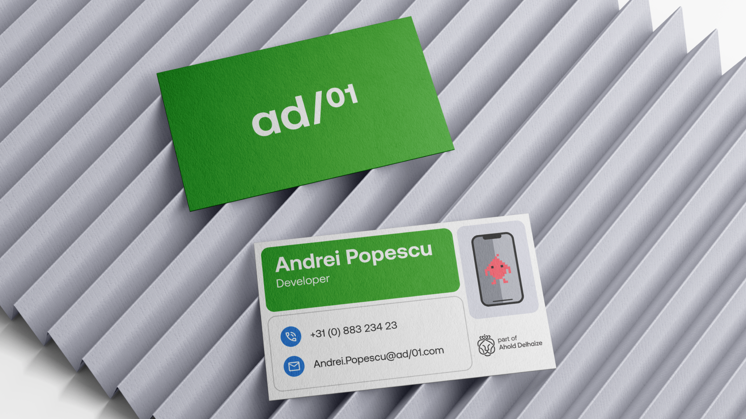Two business cards on ribbed gray surface: green "ad/01" card and white card reading "Andrei Popescu, Developer" with contact icons.