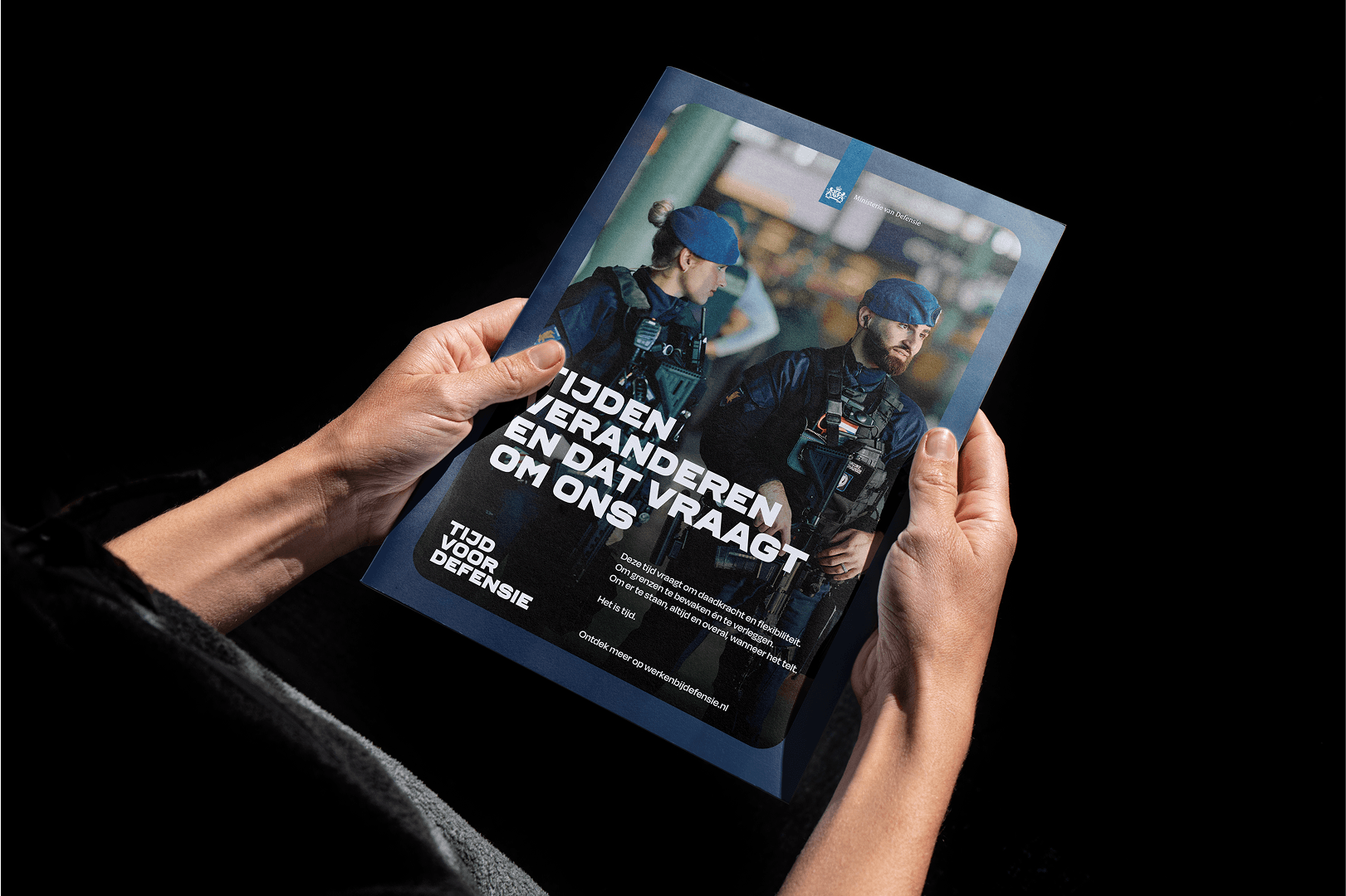 Hands holding a brochure featuring two uniformed officers in berets and tactical vests, with Dutch text on the cover