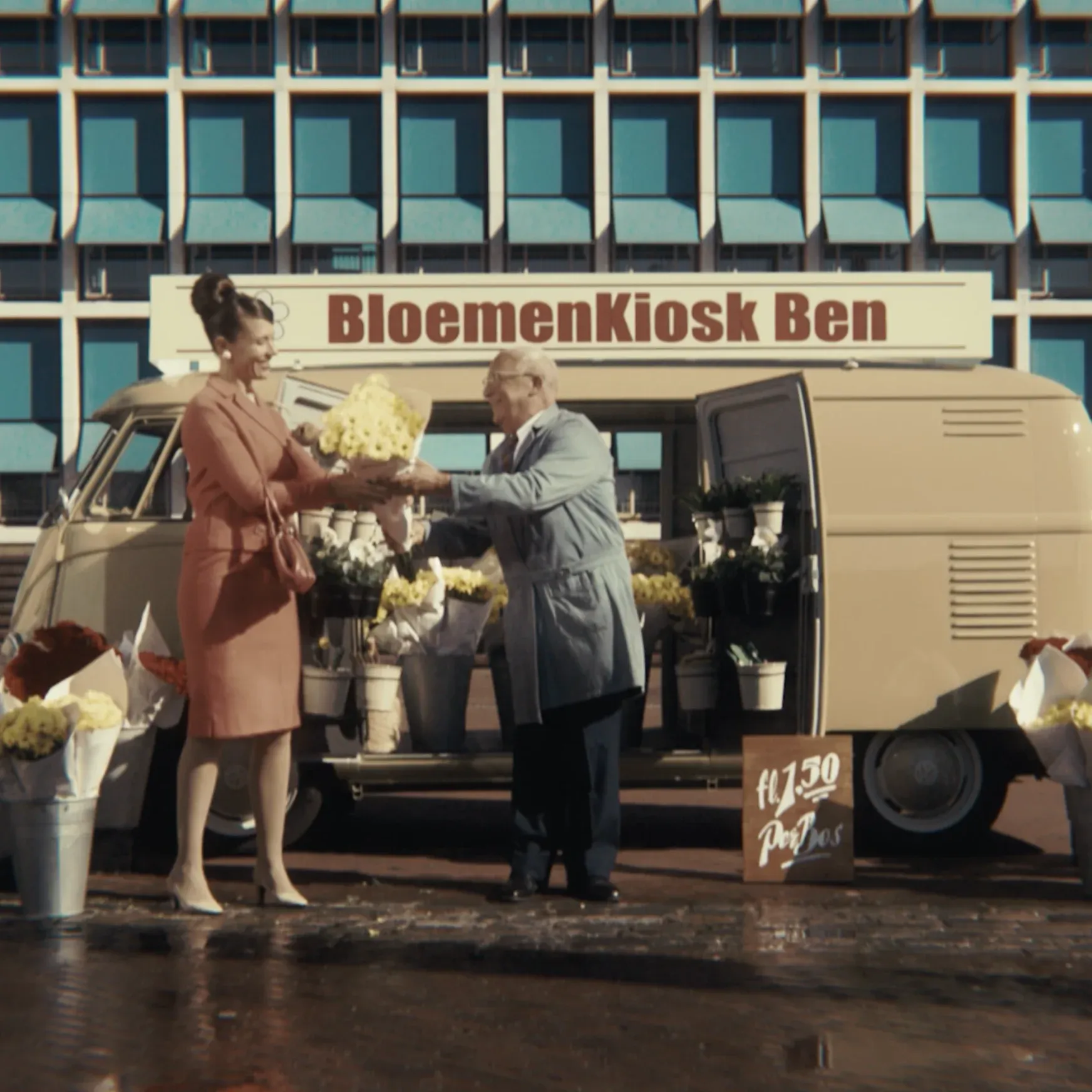An older man in a blue shop coat hands a bouquet of yellow flowers to a woman from the back of a beige vintage Volkswagen van labeled "BloemenKiosk Ben".
