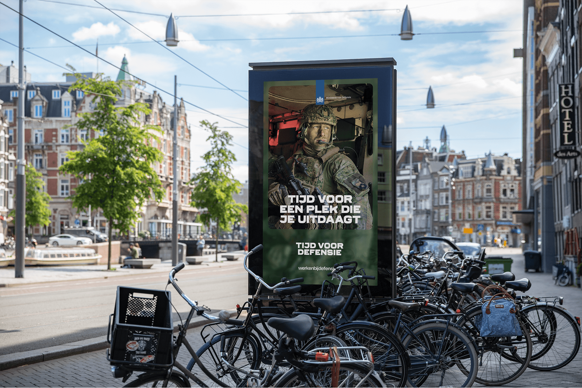 Urban street with parked bicycles and a digital kiosk displaying a recruitment poster of a soldier.