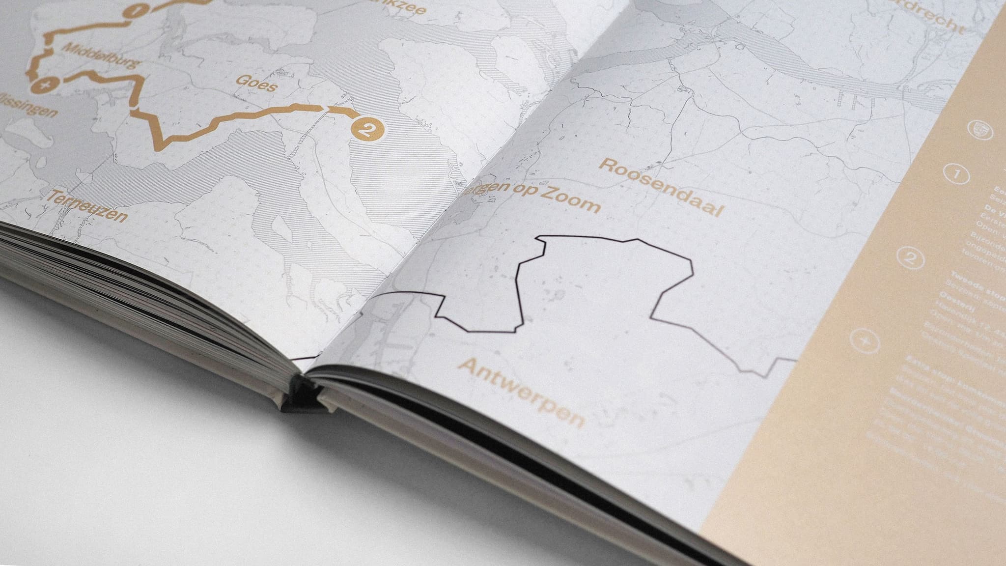 Close-up of an open guidebook showing printed maps with route lines and place names, including "Antwerpen."