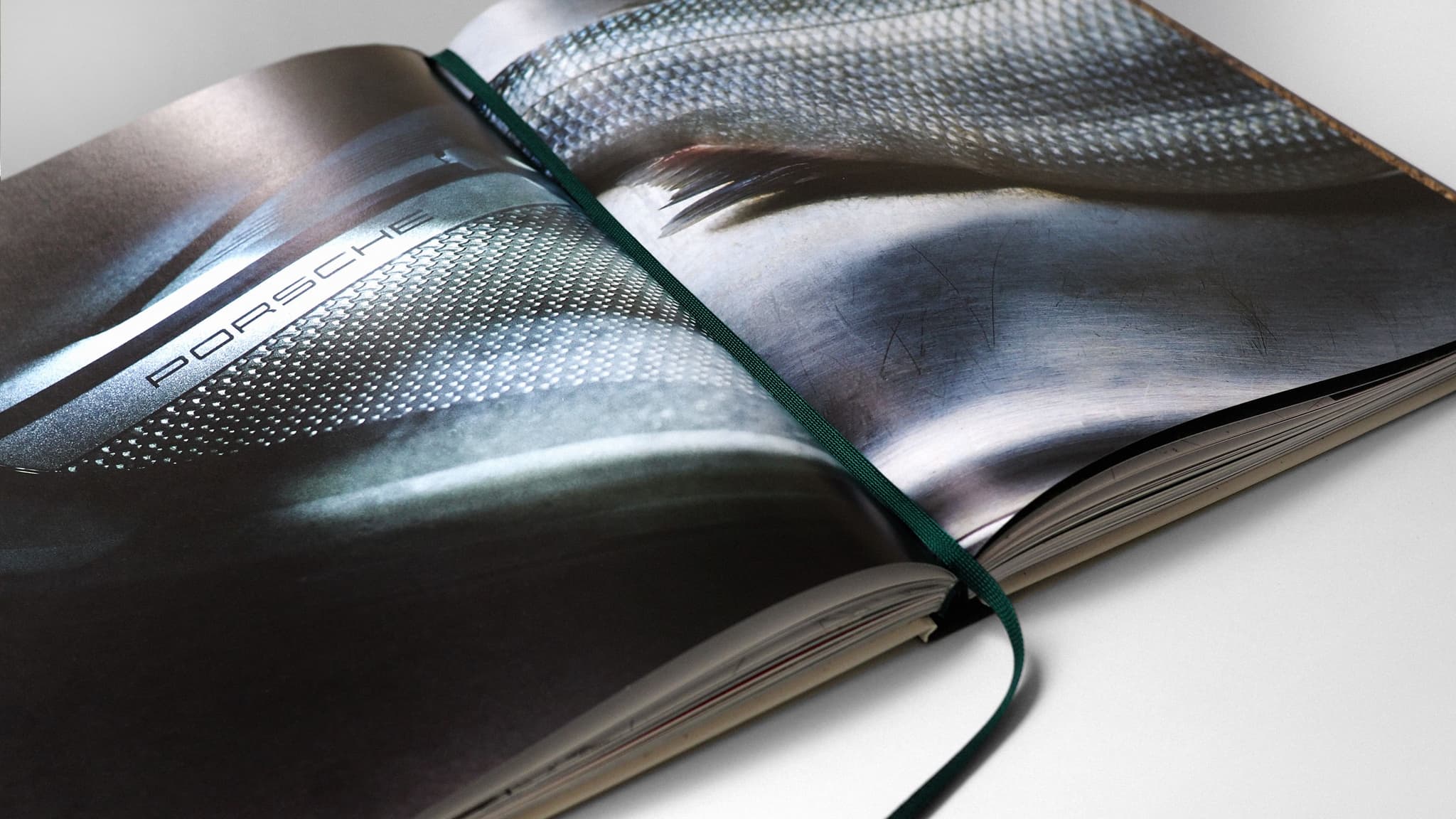 Open glossy Porsche brochure showing metallic car surface detail and a green ribbon bookmark.