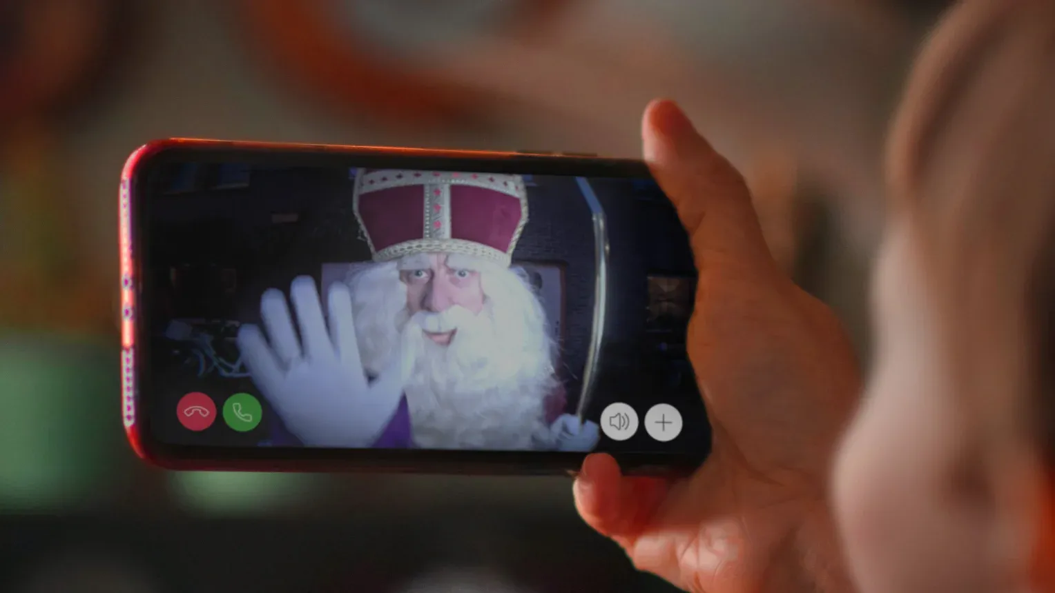Smartphone held horizontally showing a video call with Sinterklaas waving.