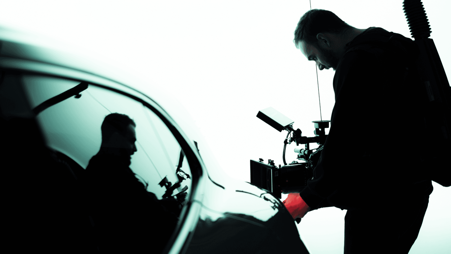 Silhouetted camera operator filming a glossy Porsche, his reflection visible in the car window.