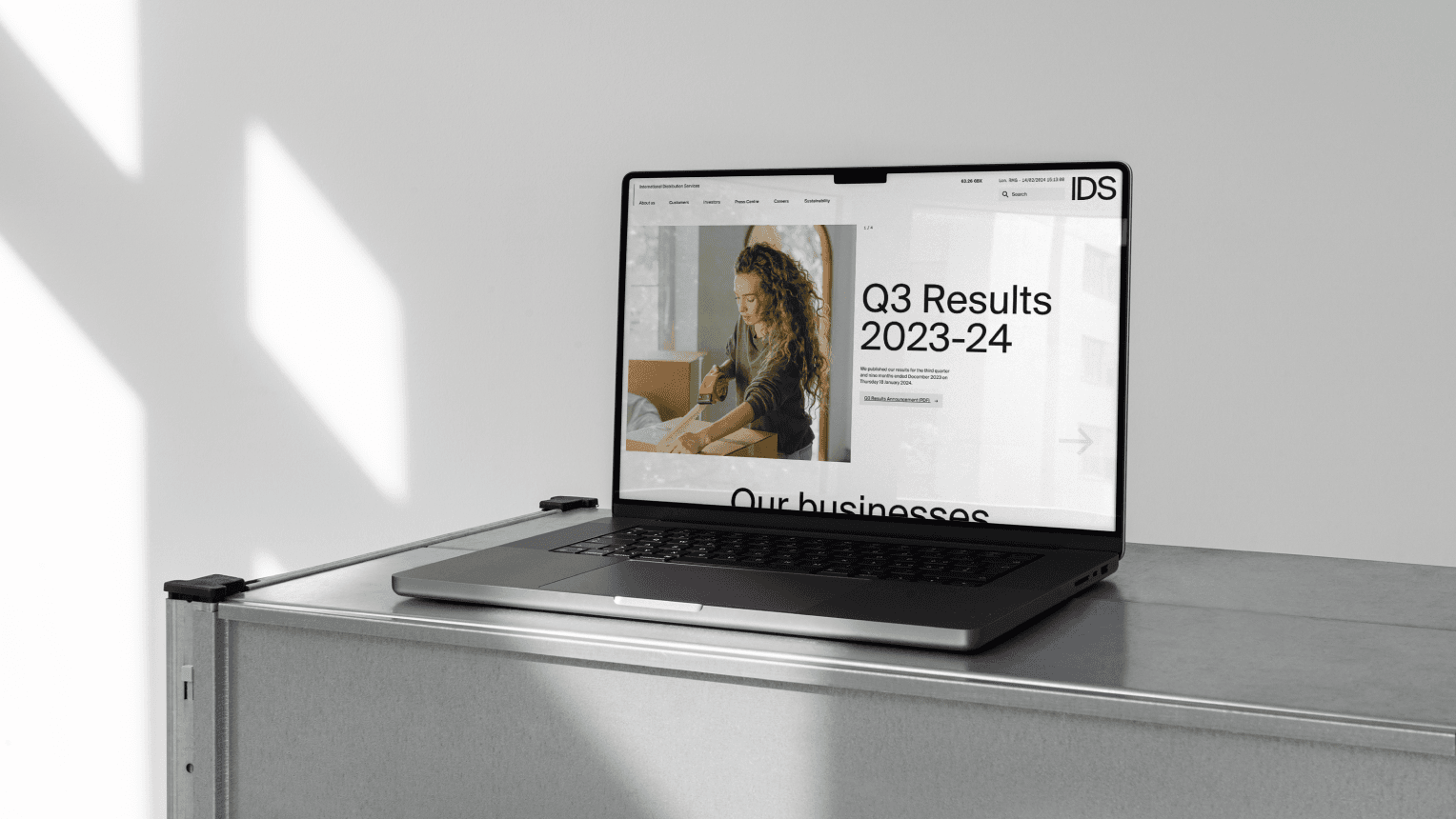 Close-up mockup of a laptop displaying the "IDS" website, showing the Q3 Results for 2023-24 and a photo of a woman packaging a box.
