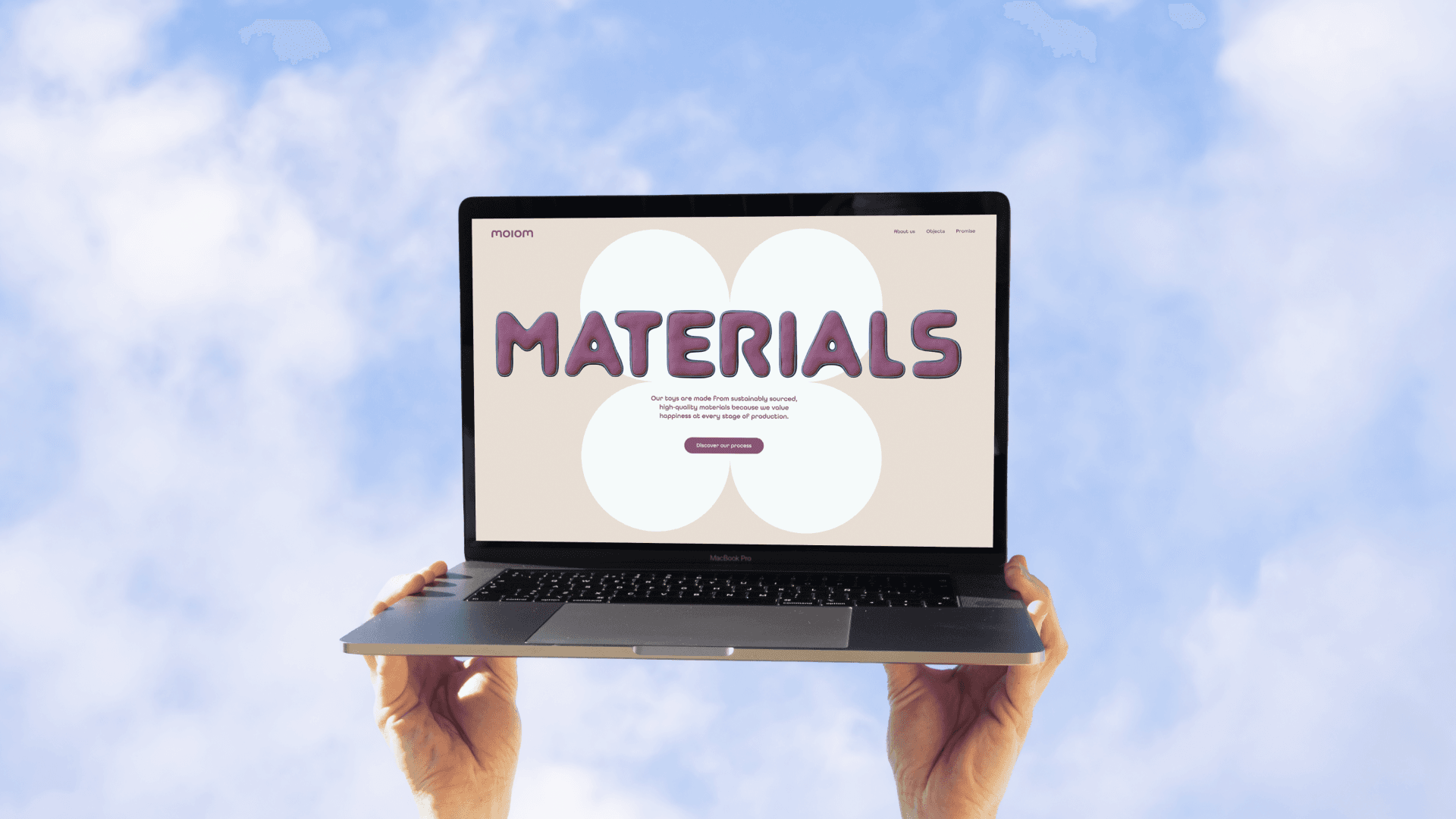Two hands hold a laptop against a blue sky; screen shows a cloud graphic and the word MATERIALS in purple bubble letters.