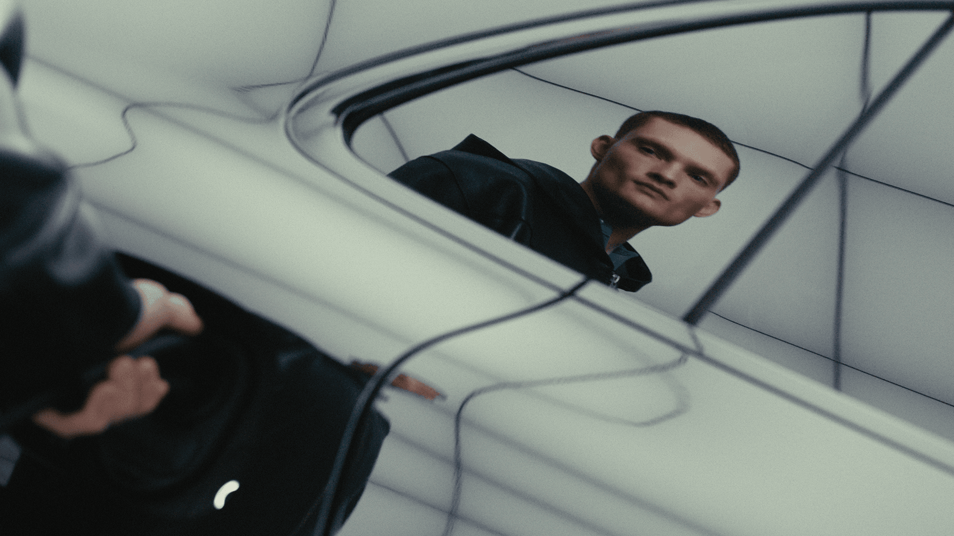 Man’s reflection in a glossy Porsche door as a hand inserts an electric vehicle charging plug