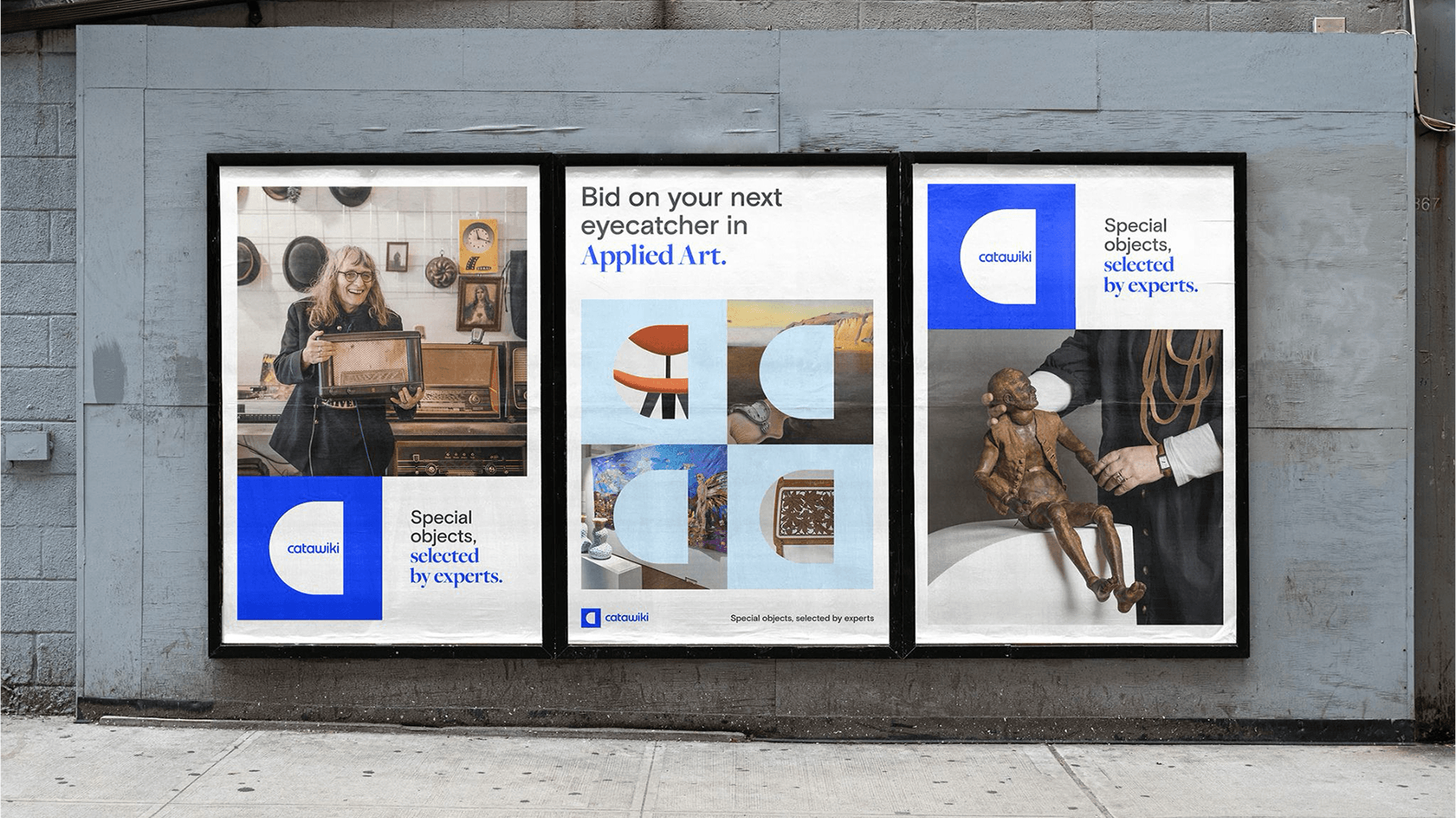 Three framed auction posters on a gray wall: woman with framed art, applied‑art collages, and a hand holding a wooden puppet.