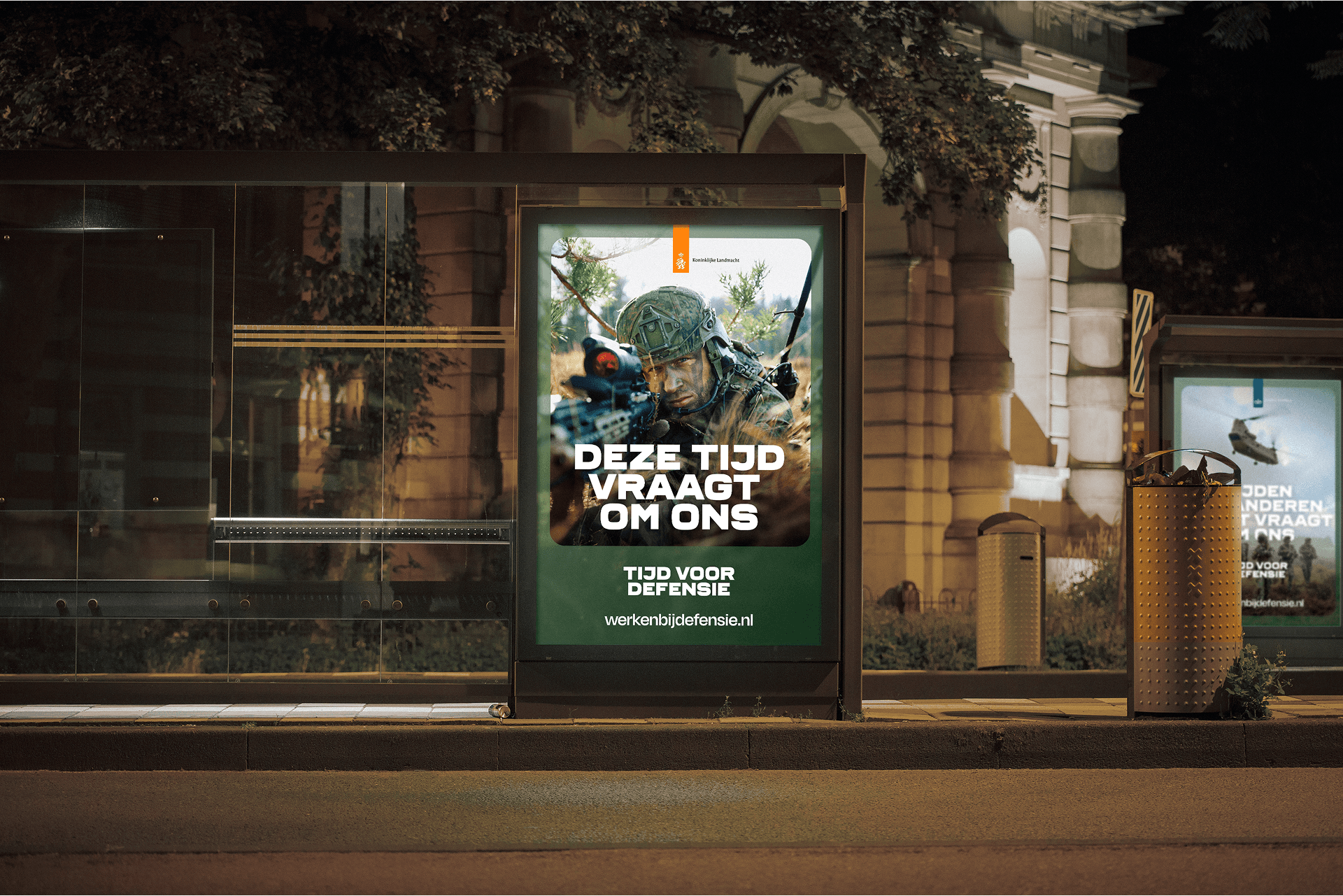 Nighttime bus stop with illuminated recruitment poster of a camouflaged soldier aiming a rifle, Dutch text visible.