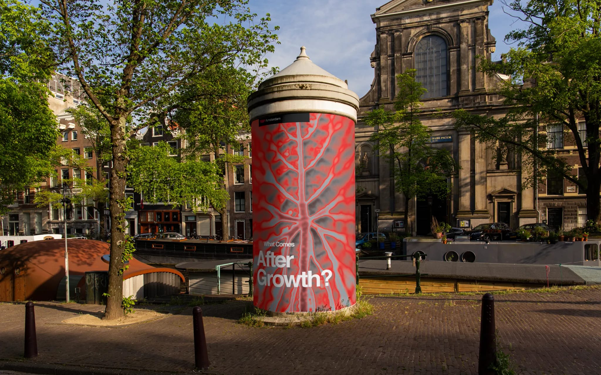 A large red cylindrical structure with tree-like patterns and text reading "What Comes After Growth?" stands near a historic building in Amsterdam.