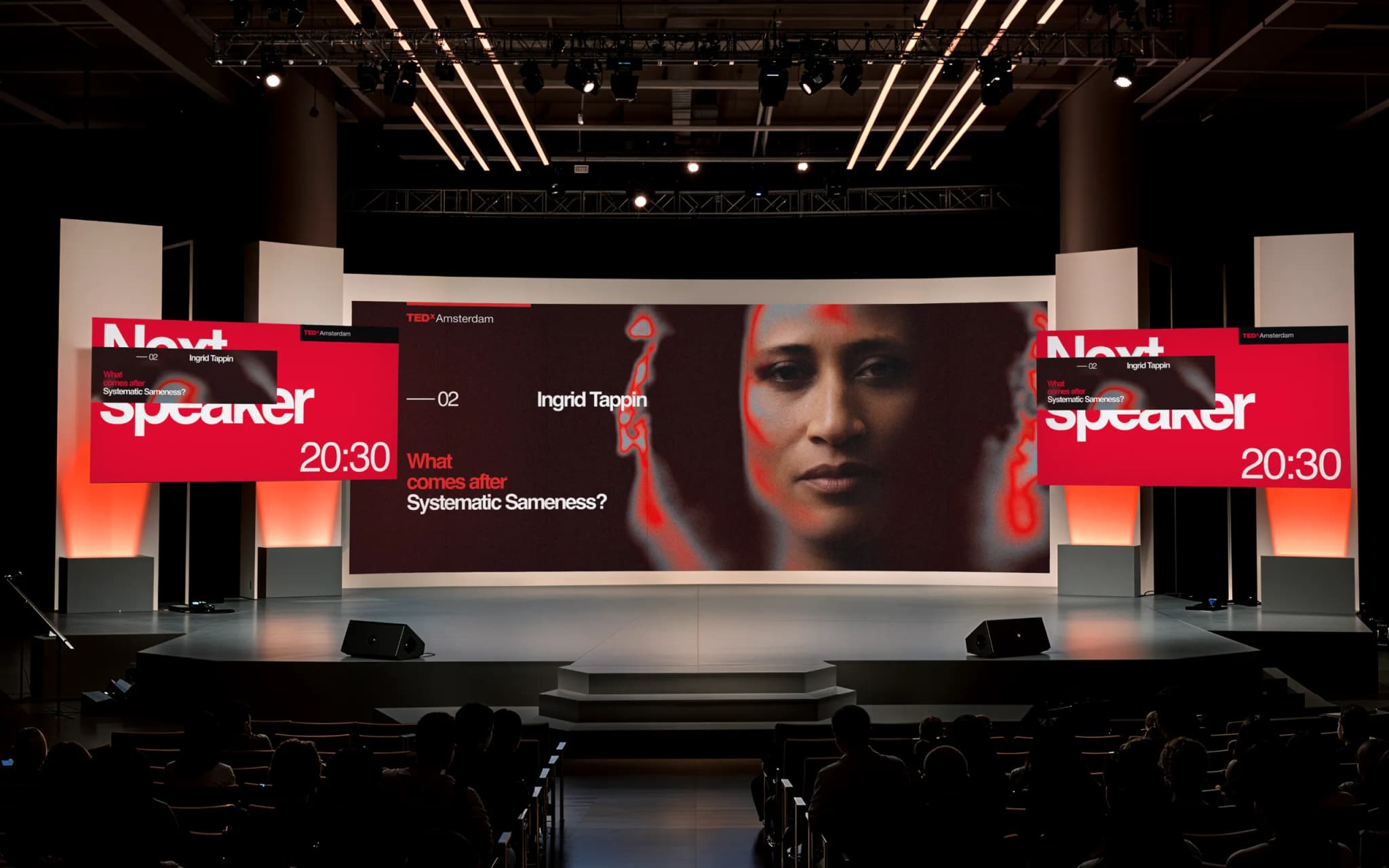 A TEDx stage with a large screen displaying a woman's face and text "What comes after Systematic Sameness?" The next speaker is Ingrid Tappin.