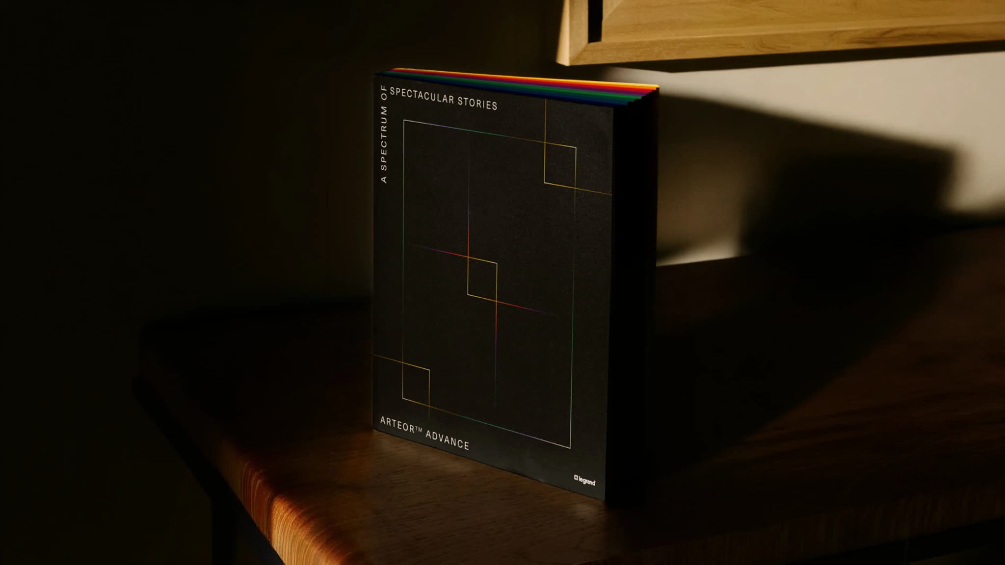 A book titled "A Spectrum of Spectacular Stories" with a black cover and colorful edges, standing on a wooden surface in dim lighting.