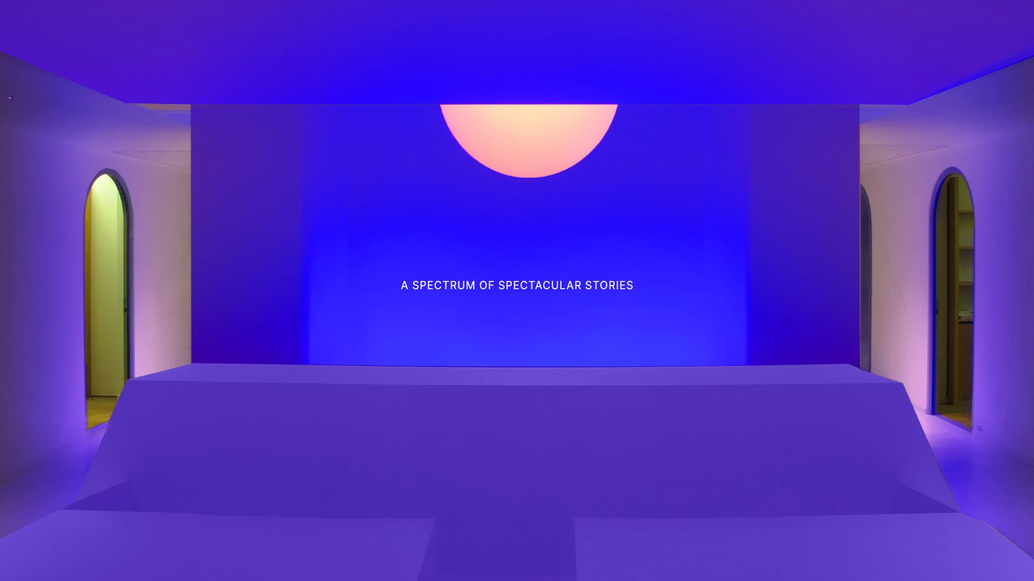 A modern room with a blue-lit stage and a large pink semi-circle above. Walls feature two open arched doorways glowing with ambient light.