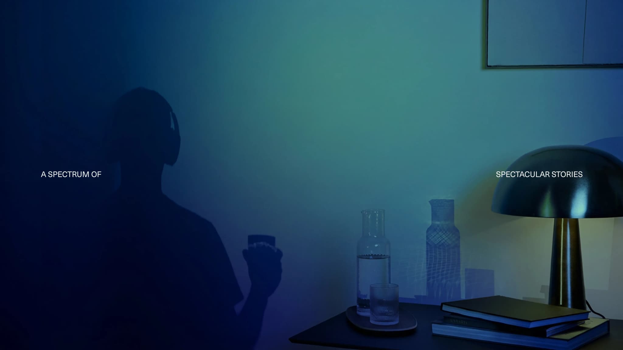 A dimly lit room with a silhouette of a person wearing headphones. A lamp, books, and a water carafe are on the table. Text reads "A Spectrum of Spectacular Stories."